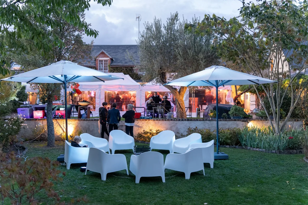 Le jardin de la fête des 100 ans de Mémé à la tombée du jour : chapiteaux blancs, parasols et salon de jardin devant la maison, dans la vallée du Loir