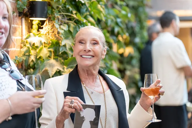 Une invitée habillée en noir et blanc sourit en montrant sa silhouette, une coupe de champagne à la main