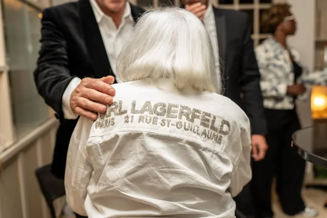 Mémé, de dos, dans sa chemise blanche Karl Lagerfeld, embrassée par un invité